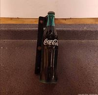 Full view of Coca-Cola bottle handle attached to black bracket