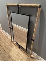 Full view of mirror leaning against wall showing rope-wrapped outer frame and inner mirror section