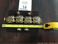 Gold-toned bracelet with intricate floral design and two pairs of gold-toned earrings, one pair clip-on and one pair screw-back, displayed with measuring tape.
