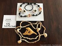 Photo of assorted jewelry including beaded black stone necklace, matching clip-on earrings, carved dolphin broach, and shell bead necklace.