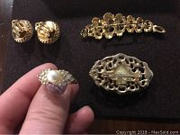 Close-up of ring, oval brooch, textured clip-on earrings and floral brooch laid on black felt background.