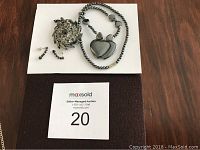 Grey stone heart-shaped pendant necklace, silver-toned long necklace, pair of pierced stone earrings, and vintage dark grey stone brooch displayed on surface.