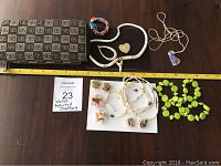 Full lot displayed on table including wallet, necklaces, earrings, brooch, and bracelet. A yellow tape measure for scale shows wallet approx. 8 inches.