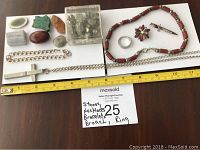 Full view of lot laid out on table with measuring tape showing scale. Includes stones, two necklaces (chain cross and beaded), bracelet, ring, and two broaches.