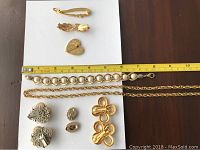 Top view of assorted vintage gold-tone costume jewelry including clip-on earrings, broaches, bracelets, and necklaces laid out with measuring tape for size reference.
