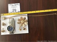 Photo showing quartz men's wristwatch, vintage flower broach, two pairs of screw back earrings, and blue stone necklace with measuring tape for size reference
