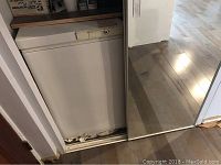 Full view of the white Woods chest freezer in a room with light wood flooring and adjacent door.