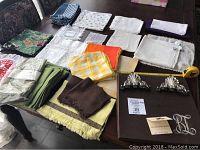 Full assortment of linens including boxed Browns Linen bridge table cloth, assorted napkins, napkin rings, tea cozy on a table.