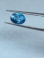 Gemstone held in tweezers showing top facets and color