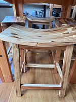Multiple wooden saddle stools nested together showing seat curvature and leg construction