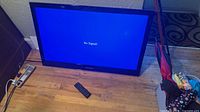 Dynex 32" TV on floor displaying No Signal with remote and power cord nearby