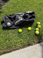 Black ITECH duffel bag with six yellow softballs shown outdoors on grass