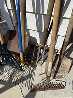 Group of rakes, cultivator, pitchfork, shovels and edger leaning against wall