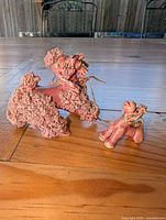 Mother and puppy pink spaghetti poodle ceramic figurines connected by gold chain on wooden table