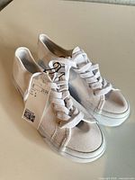 Pair of white canvas sneakers with laces and tag visible