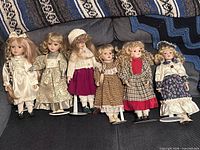 Group shot of all six porcelain dolls on couch with stands