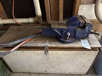 Side view of blue bench vise with crowbars on wooden surface