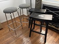 Two chrome metal stools and two black wood stools on hardwood floor