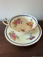 Cup on saucer showing floral pattern, blue band, gold trim, signs of crazing