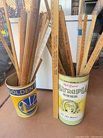 Group of wooden rulers and yardsticks inside two metal advertising containers