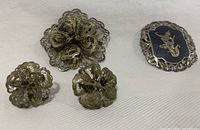 Front view of filigree brooch, matching clip-on earrings, and niello oval brooch