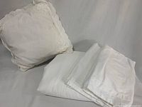 White decorative pillow with lace edge and folded white bedding pieces