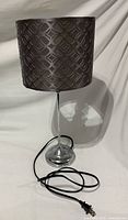 Table lamp showing chrome base, stem, patterned drum shade, power cord