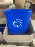 Blue plastic recycling bin with white logo standing in carton