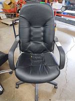 Front view of black faux leather executive office chair showing seat, backrest, armrests, and height lever tag