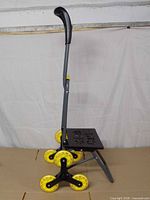 Side view of folded Climb Cart showing frame, tri-wheel clusters, platform, handle