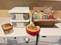 overall view two clear tubs, cardboard box, square floral tin, round red tin on appliances