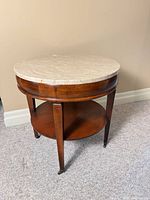 Full view of round end table showing marble top, wooden base, lower shelf and casters