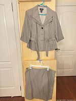 Full view of jacket on hanger above matching skirt on hanger