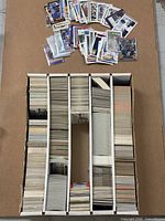 Four-row storage box filled with unsorted trading cards and loose sample cards displayed on lid