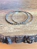 Twisted and plain sterling silver bangles on wooden surface
