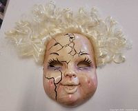 Front view showing cracked porcelain doll face design and attached blonde hair