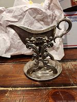 Front side view of silver-plated gravy boat showing ornate pedestal and handle