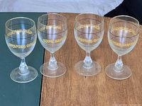 Front view of all four clear glass goblets with gold lettering and rim