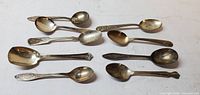 Top view of nine assorted silver-tone teaspoons showing different handle patterns and tarnish