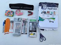 All items laid out including paper ream, hole punch, writing instruments, scissors, tape dispenser, stapler, math set