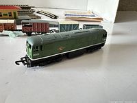 Side view of green diesel locomotive numbered D5000 with freight wagons and track visible behind
