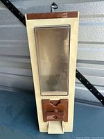 Front view of Versavend dispenser showing cream body, brown coin mechanism, clear hopper