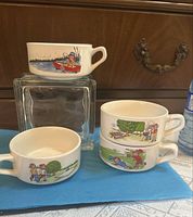 Four handled soup bowls showing different Campbell's Soup Kids summer scenes