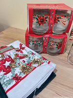 Two boxed sets of poinsettia old-fashion glasses with loose glasses and folded tea towels