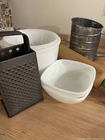 Group view of milk glass bowls, metal grater, flour sifter, rolling pin