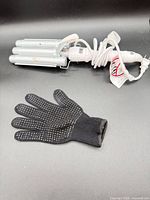 Curling iron coiled with cord and glove in foreground
