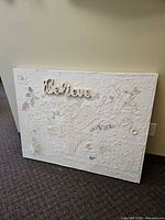 Front view of canvas showing word "Believe," texture, floral decoupage