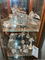 Two cabinet shelves filled with various crystal figurines and bell
