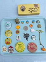 Overview of entire lot on tray showing tin, buttons, wooden tokens, badges, patch and charm