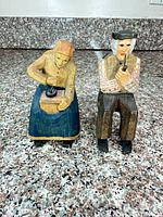 Front view of both seated wooden figurines showing carving details and paint